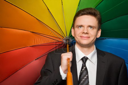 Smiling businessman in suit with multi-coloured umbrella