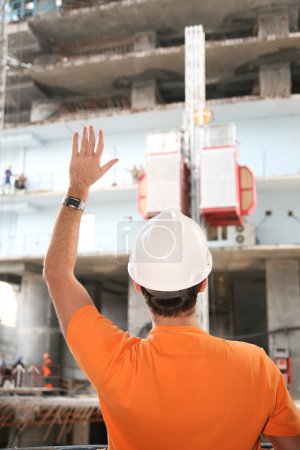 Behind worker in the helmet with hand up