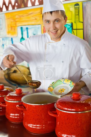 Cheerful cook in uniform spoon imposes soup in plate in public c