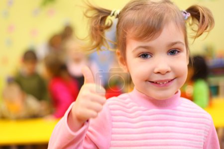 Little smiling girl in kindergarten shows sign ok