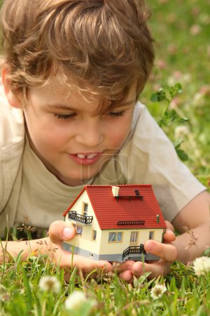 Boy lies in grass with house model in hands