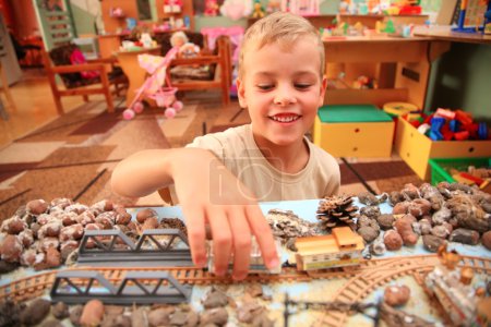 Boy plays with toy railroad in playroom
