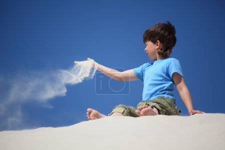 Boy sits on sand and scatters it