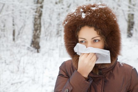 Young woman with scarf blowing nose in wood in winter