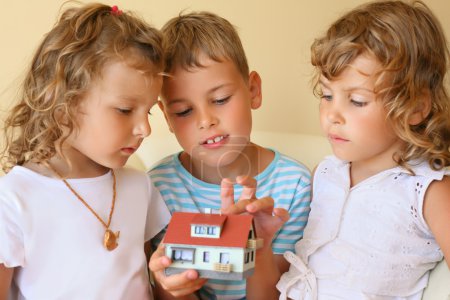 Children three together keeping in hands model of house in cosy