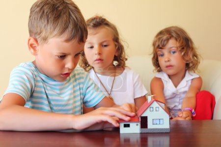 Children three together looking at model of house standing on ta