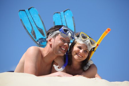 Young pair in fins and underwater masks lies on sand