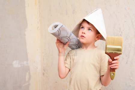Boy with brush and roll of wallpaper in papper hat