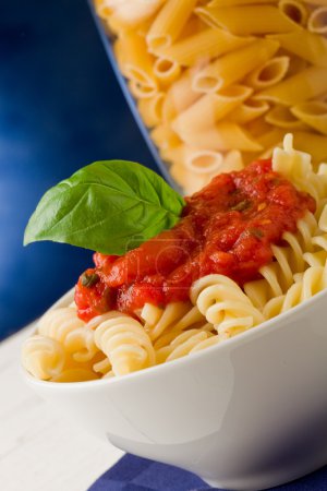 Pasta with tomato sauce and basil on blue background