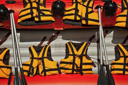 Rafting equipment is presented at the city fair. Yellow lifejackets on red inflatable boat background.