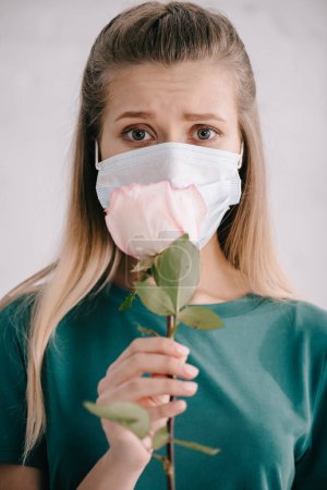 selective focus of blonde woman in medical mask holding rose in hand