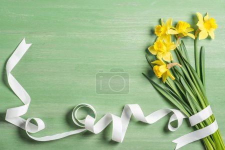 view from above of bouquet of daffodils wrapped by white ribbon on green background