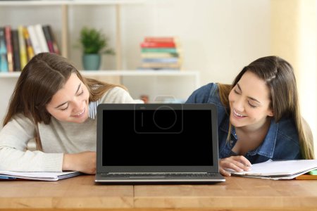 Two happy students watching a laptop mockup screen on a desk at home
