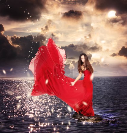 Girl in Red Dress Standing on Ocean Rocks