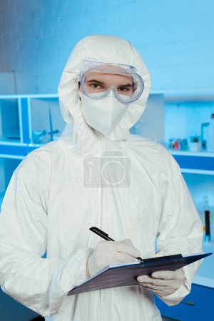 scientist in hazmat suit and goggles holding clipboard and pen 
