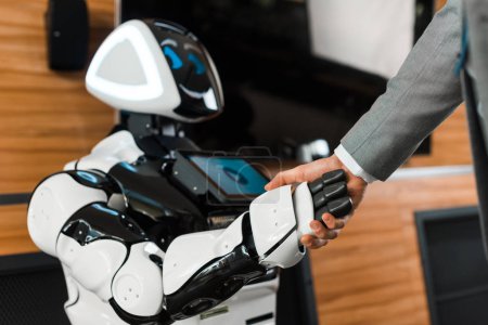 cropped view of businessman shaking hands with smiling robot in office