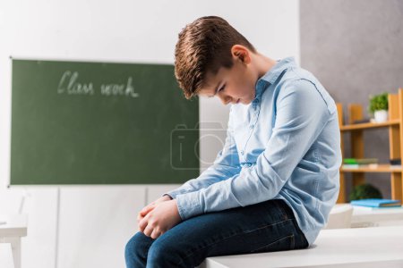 sad and bullied schoolchild sitting on table in classroom 