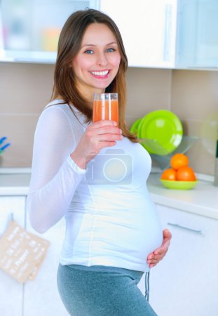 Pregnant Young Woman drinking Fresh Juice at home kitchen