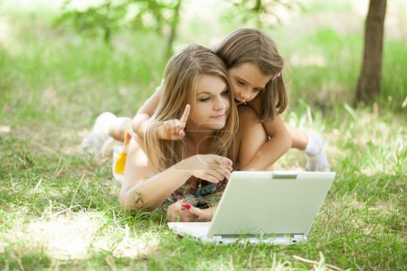 Two sisters with laptop in the park.